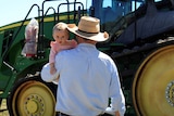 Burly farmer carries baby towards tractor