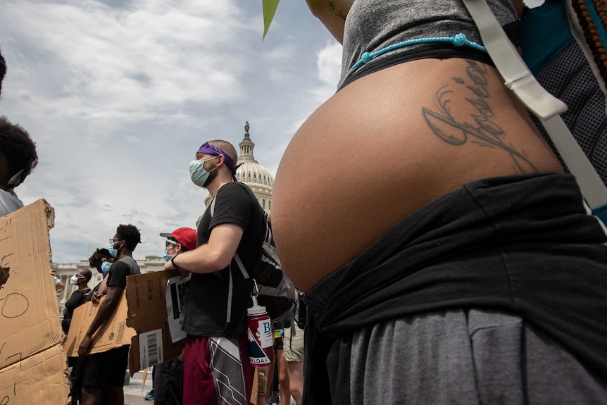 A woman's pregnant belly in the foreground with the US capitol building in the background