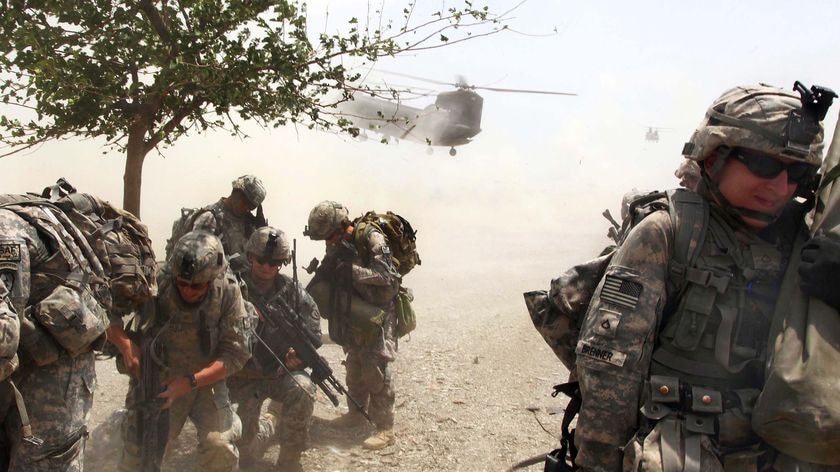 United States soldiers duck as a Chinook helicopter lands