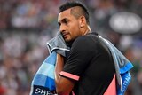 Nick Kyrgios in a black and pink shirt wipes his face with a towel with the crowd in the background