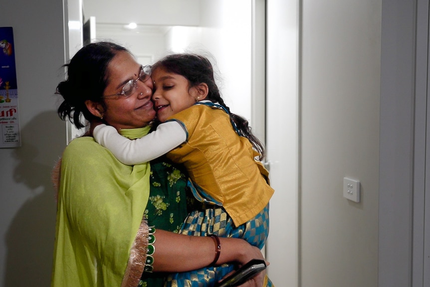 Akila hugs her young daughter, who is hugging her around the neck.