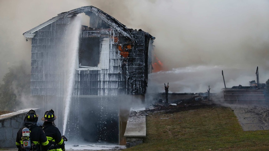 Firefighters hose down a blackened house as they try and extinguish the flames inside