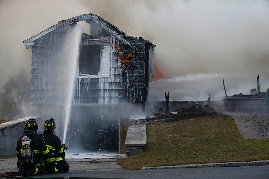 Firefighters hose down a blackened house as they try and extinguish the flames inside