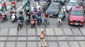 A Vietnam traffic policeman stands in front of waiting motorbikes and cars.