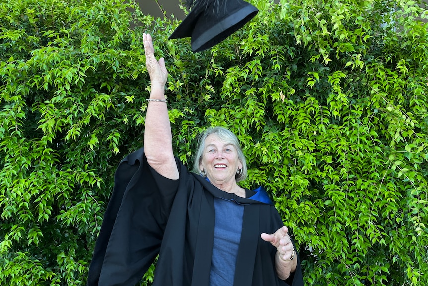 smiling woman in black graduation gown tosses black hat into air in celebration