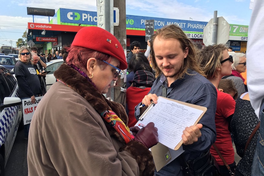 A man holds a clipboard with a petition on it as a woman signs it outside the Preston market.