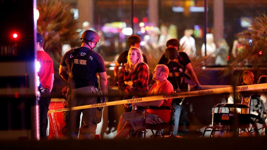 Behind police tape, authorities talk to a group of people.