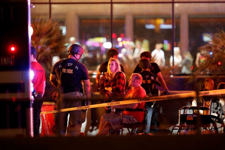 Behind police tape, authorities talk to a group of people.