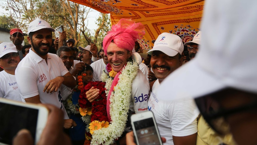 Pat Farmer laden with garlands of flowers and wearing a pink turban among supporters.