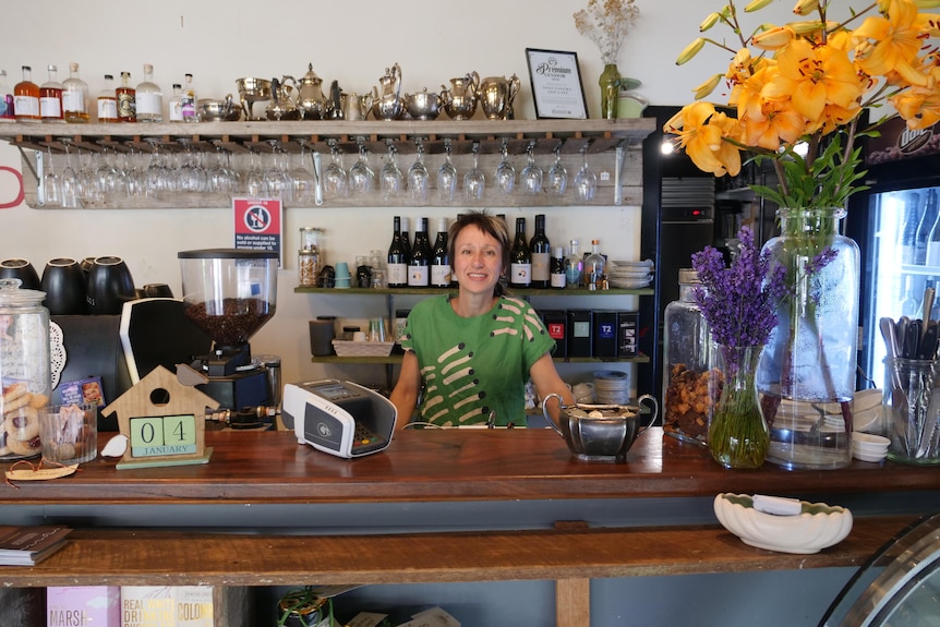 Woman in green shirt stands behind cafe counter.