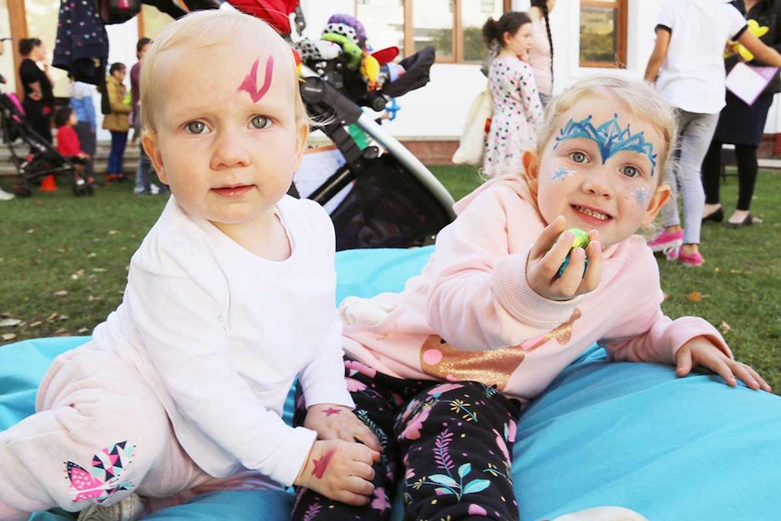 Two young girls sit on a mat holding Easter eggs.