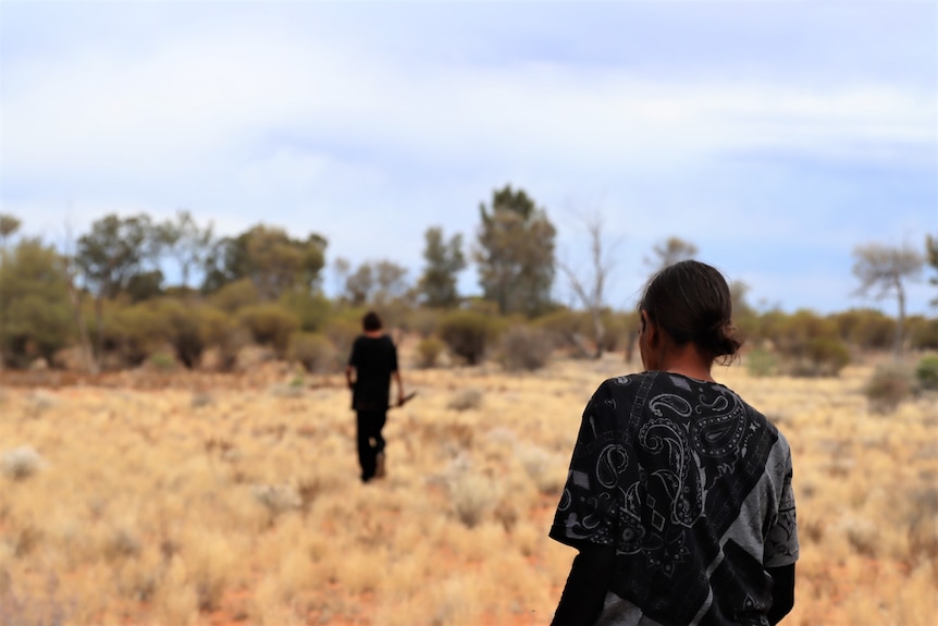 Two women walk away from the camera on light scrubby yellow grass