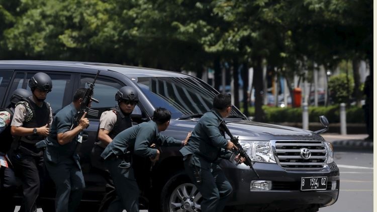 Indonesian police hold rifles while walking behind a car for protection after an explosion blasted a police building.