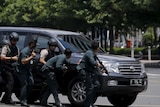Indonesian police hold rifles while walking behind a car for protection after an explosion blasted a police building.