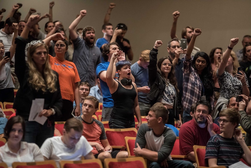 Protesters raise their fists in protest towards the front of a lecture theatre.