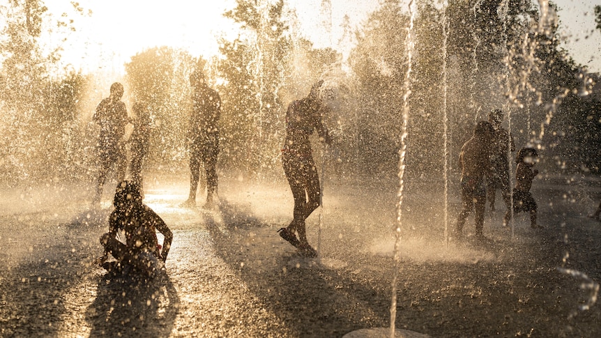 Silhouettes of children playing in water at a fountain in Athens during a heatwave with the sun behind them