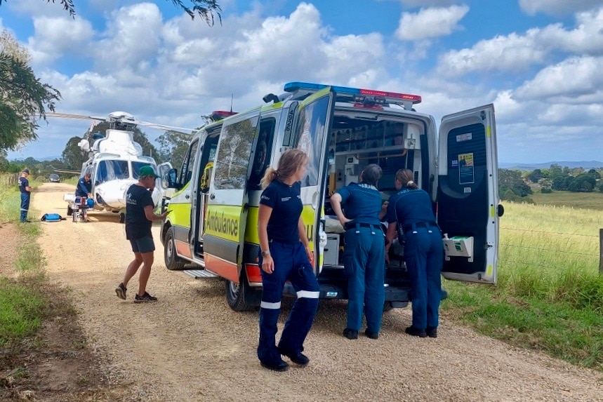 Paramedics looking at  patient in an ambulance with a helicopter on the road behind them.