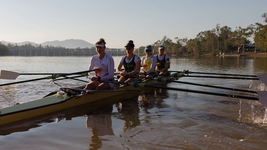 Four women in a rowing boat with barrage in the background