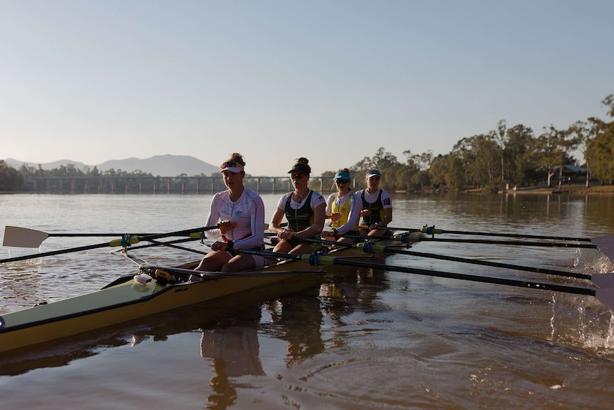 Four women in a rowing boat with barrage in the background