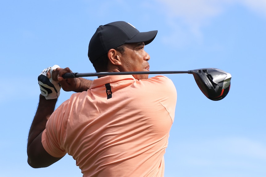 A man in a baseball cap looks right of frame with a golf club over his shoulder.