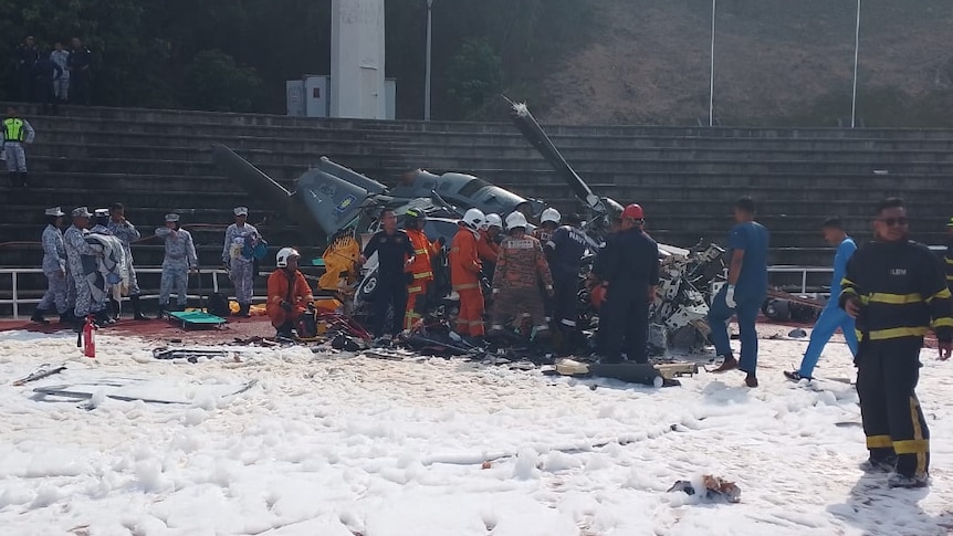 A view from afar showing people crowded around a helicopter that has crashed.
