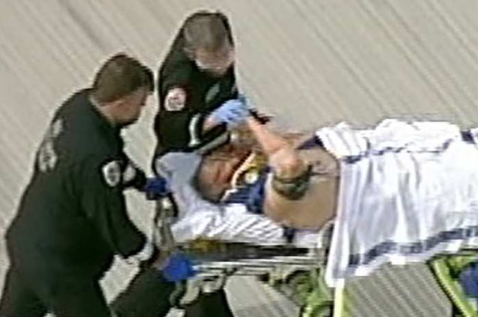 Tony Mokbel shakes hands with a paramedic as he is wheeled into hospital on a stretcher.