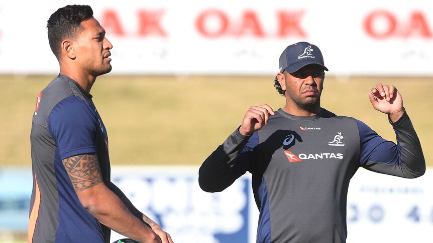 Israel Folau holds a rugby ball as Kurtley Beal stretches alongside him.