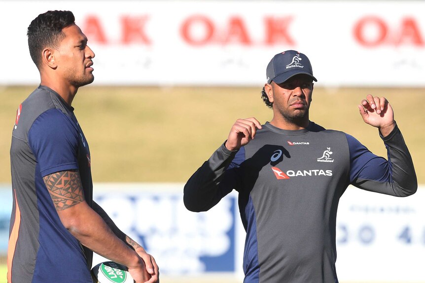 Israel Folau holds a rugby ball as Kurtley Beal stretches alongside him.