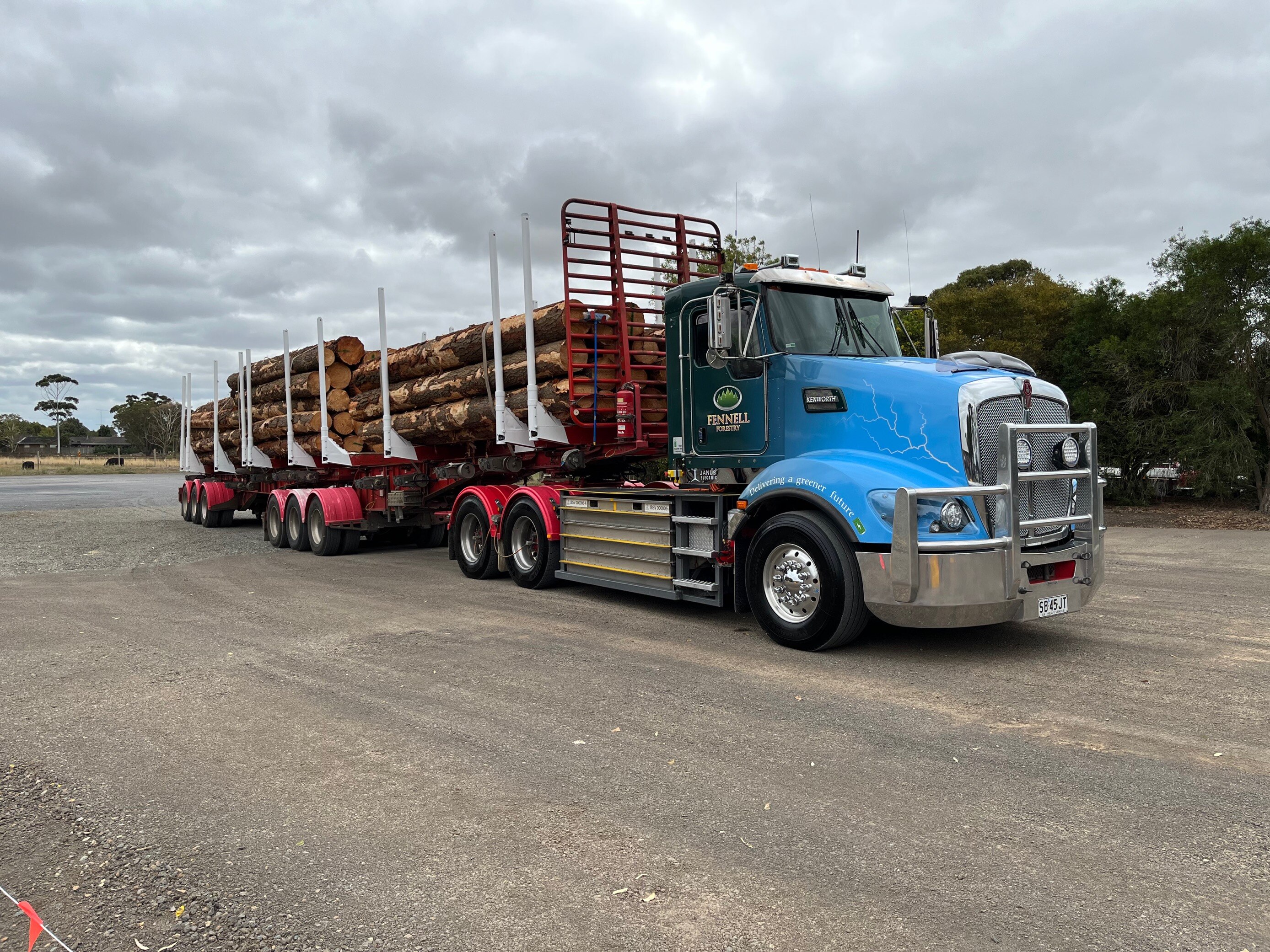 En un aparcamiento hay un gran camión que transporta decenas de troncos cortados. 
