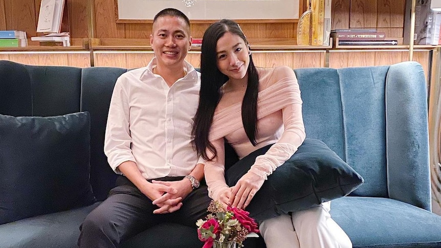 A Thai man and a Thai woman sit together smiling on a couch 