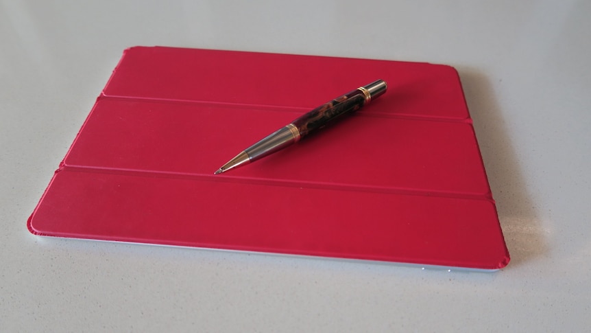 An iPad with a red cover and a pen on top.