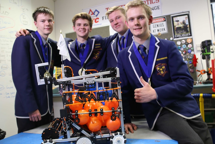 High school students standing in a row a round a robot they built