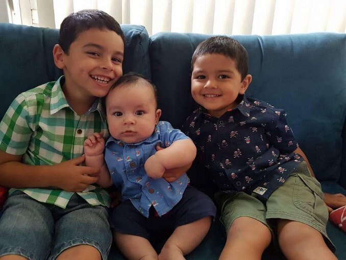 A young Jamahl sitting on the couch with his two younger brothers, one is just a baby sitting in his lap. 