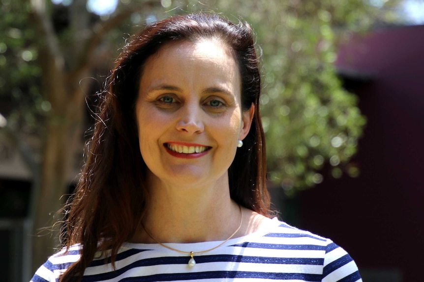 A woman with long dark hair and a stripy top smiles at the camera.