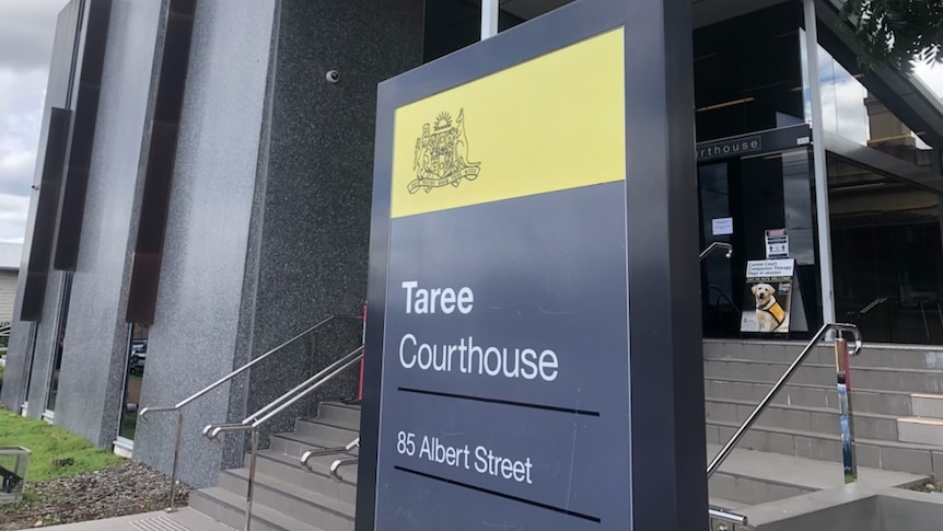 A sign that says "Taree Courthouse" outside a dark-coloured building beneath a grey sky.