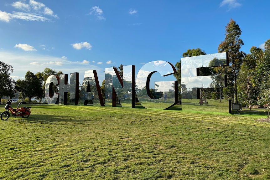 A large-scale mirrored installation set up in harbour parkland which reads "CHANGE" 
