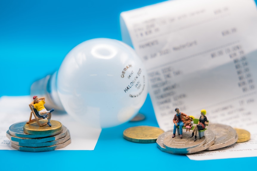 A photo of miniature people standing next to light bulbs.