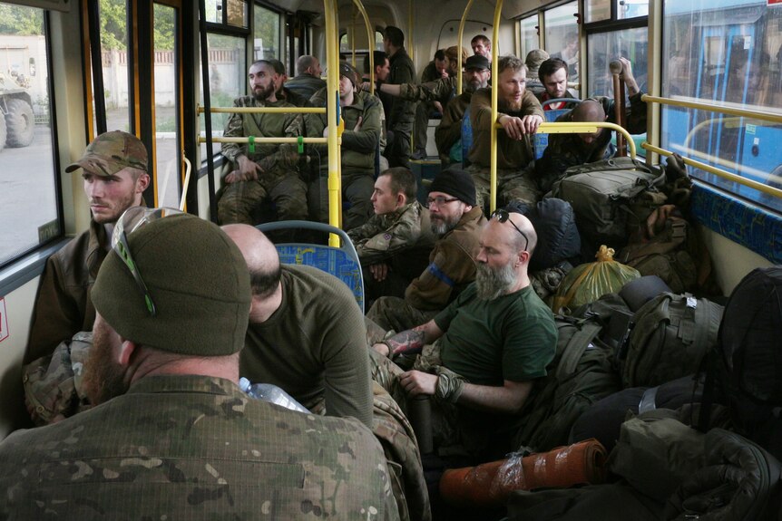Men in green army fatigues look exhausted inside bus.