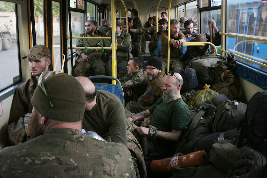 Мужчины в зеленой армейской форме внутри автобуса выглядят уставшими.