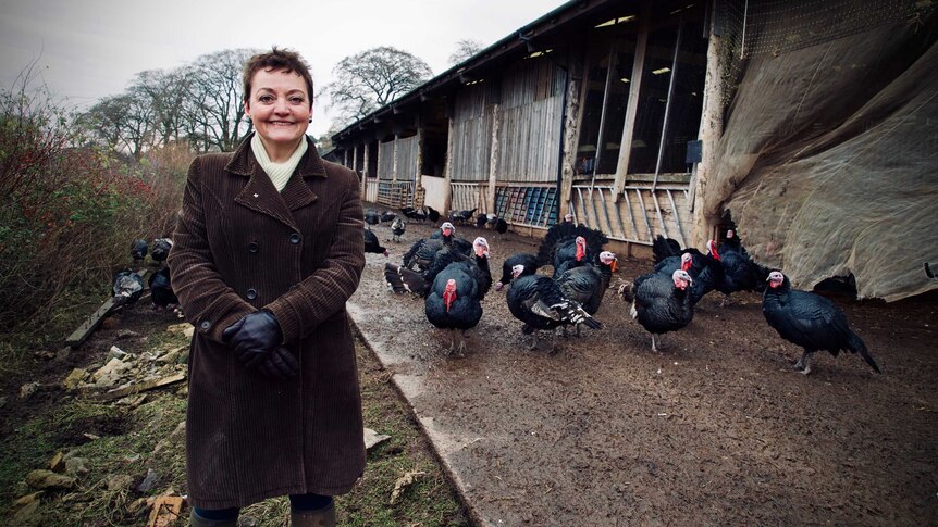 Farmer Heather Anderson stands in front of turkeys and a farm shed.