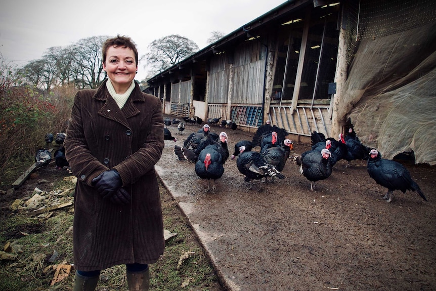 Farmer Heather Anderson stands in front of turkeys and a farm shed.