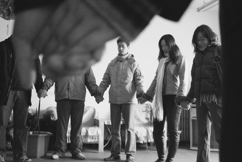 A group of young Chinese Christians hold hands in a circle to pray