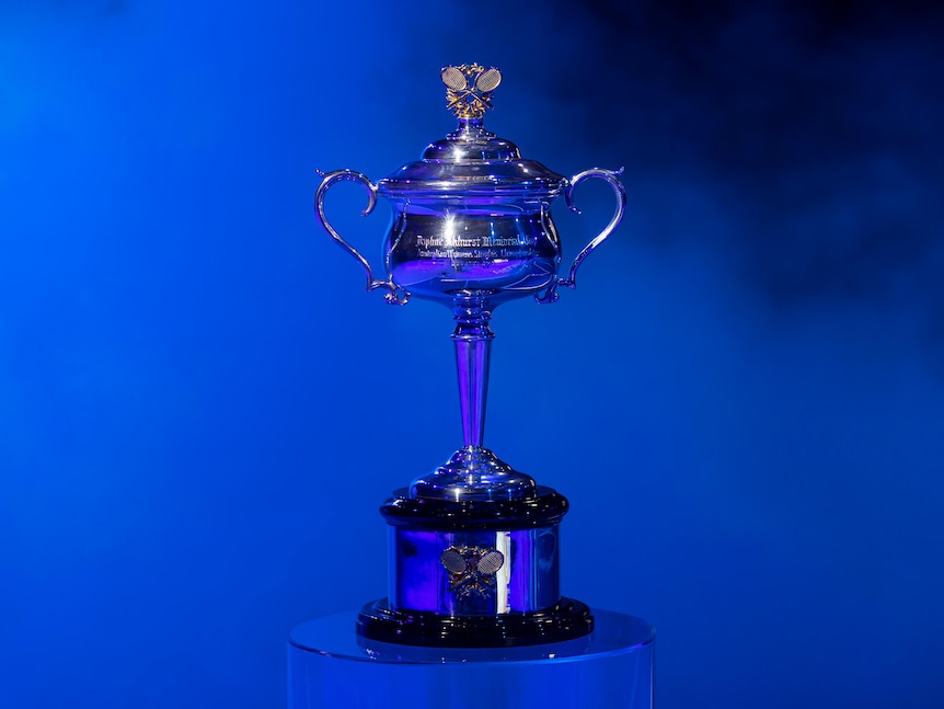 A silver tennis trophy sits against a vivid blue background at the Australian Open.