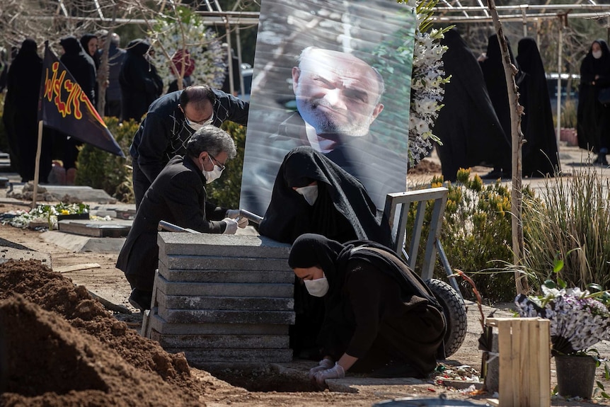 Relatives wearing face masks mourn over the grave of a man whose picture is seen behind.