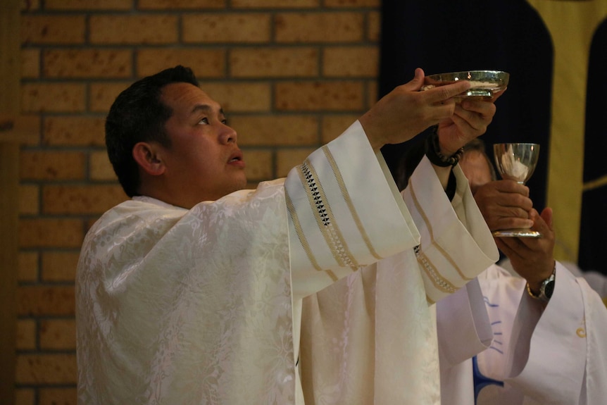 A priest holds up a silver dish in the air.