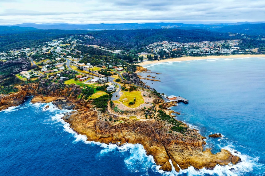 A headland surrounded by the sea, charred trees surrounding some houses.