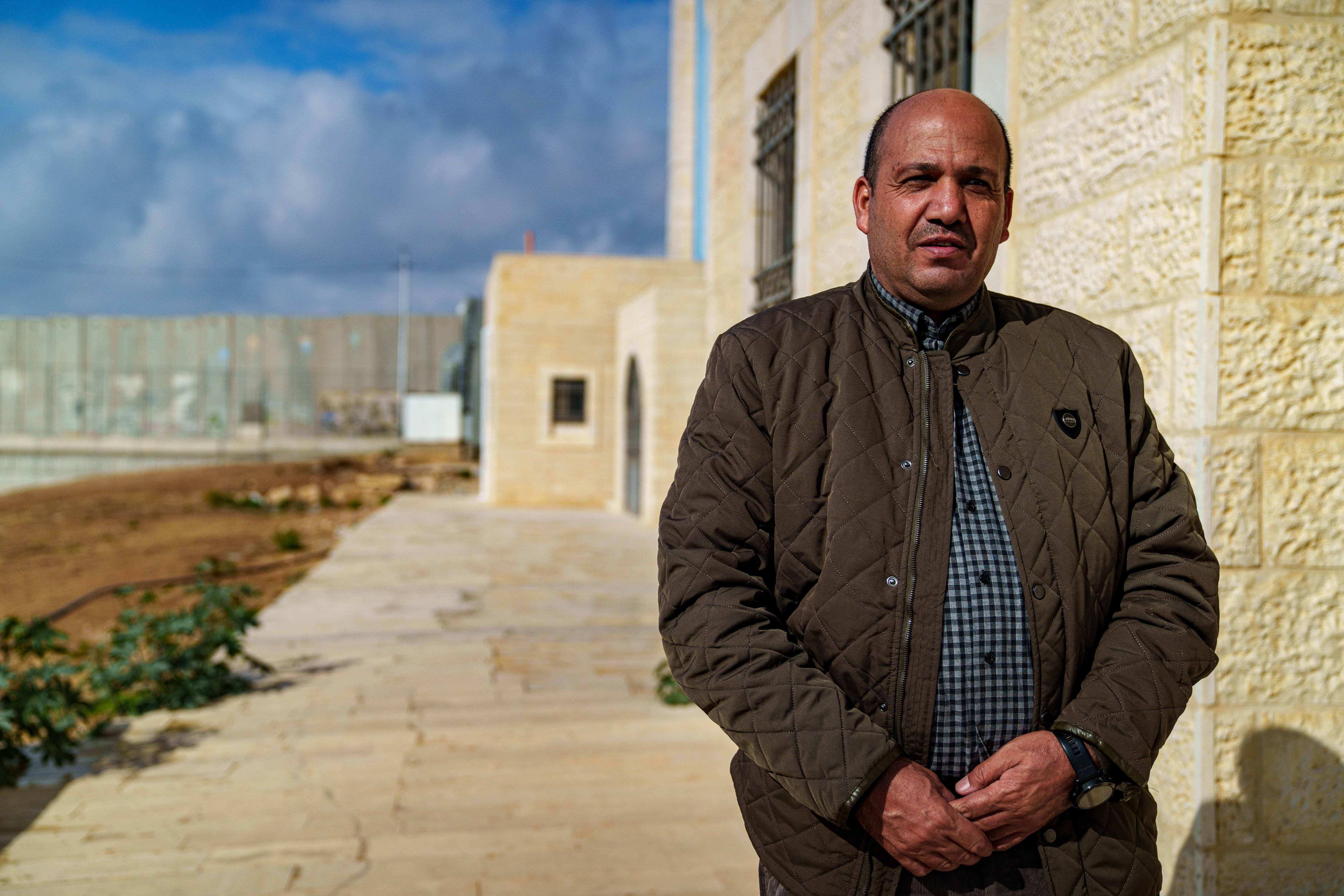 A man of Middle Eastern appearance stands next to a sandstone university building.