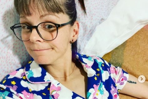 A woman wearing a floral top takes a selfie shot lying down.