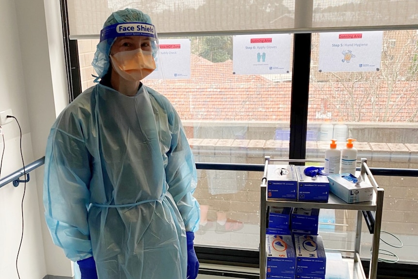 A woman in a blue plastic gown and hair cover, a mask, face shield and gloves for a story on end of life care during COVID