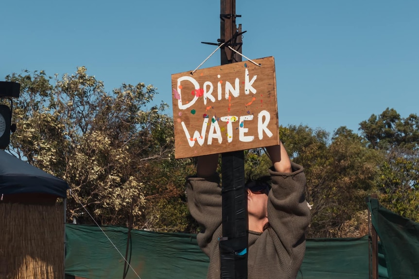 person affixing sign to pole that reads DRINK WATER 